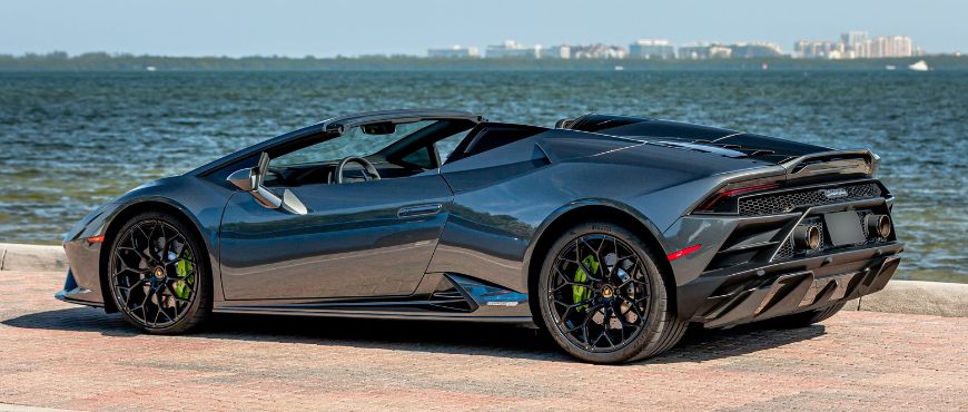 A sleek grey Lamborghini Huracán parked along Miami's seafront with the ocean and the Miami skyline in the distance