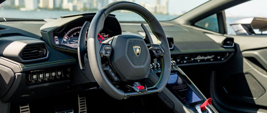 Interior view of a Lamborghini Huracán, showcasing the luxury steering wheel and dashboard with a Miami skyline visible through the windshield